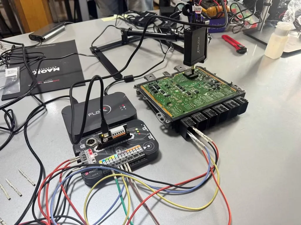 Engine control unit connected to a bench programming tool with coloured test leads on the workshop bench